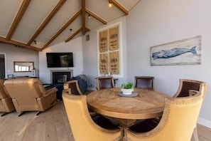 Ein geräumiges Wohnzimmer mit hoher Decke, Kamin, Fernseher und einem runden Holztisch mit Stühlen.