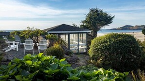 A gazebo with a glass enclosure, surrounded by a garden with various plants and shrubs, overlooking a beach with a clear sky. - Devon West (Newport)