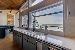 Eine Küche mit großem Fenster zum Strand, Holzschränken und einem modernen Wasserhahn.