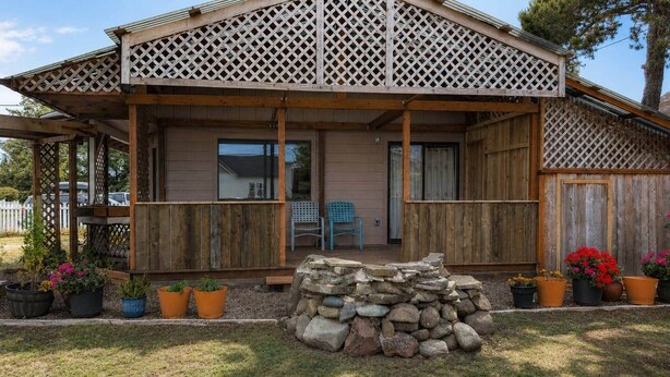 Een houten huis met een overdekte veranda, een stenen muur en potplanten.
