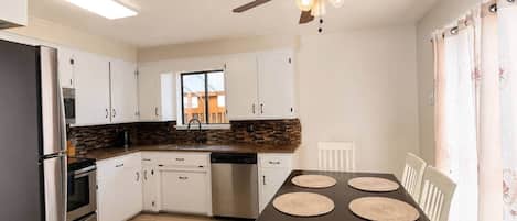A modern kitchen with white cabinets, a dark countertop, a built-in oven, and a ceiling fan.