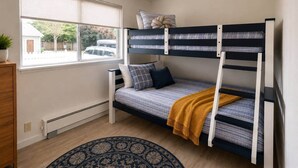 Een stapelbed met een raam, een houten dressoir en een kamerbreed tapijt met een patroon.