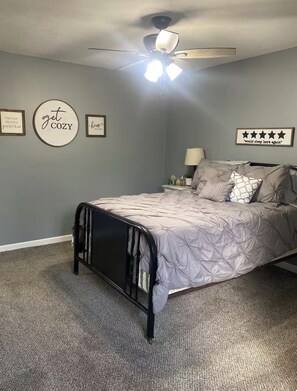 A bedroom with a bed, a ceiling fan, and wall decorations. - Cozy 1-bedroom house in wonderful Doniphan with AC (Doniphan)