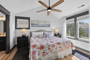 Ein Schlafzimmer mit einem Bett, zwei Nachttischen mit Lampen, einem Deckenventilator, einem Fenster mit Blick und Bildern an der Wand.