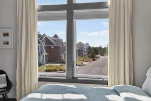 Ein Schlafzimmer mit großem Fenster, einem Bett, einem Sessel und einem gerahmten Bild an der Wand.