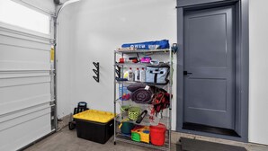 Un espace de rangement doté d’étagères où sont entreposés divers objets, une boîte de rangement noire et une porte grise.