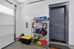 A storage area with shelves holding various items, a black storage box, and a gray door. - Dory Coastal Paradise - walk to Cape Kiwanda (Pacific City)