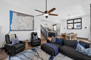 A modern living room with a large map, leather sofas, a dining area, and a kitchen in the background. - Dory Coastal Paradise - walk to Cape Kiwanda (Pacific City)