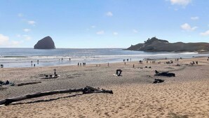 Une plage avec des gens, une grande formation rocheuse et une colline au loin.