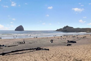 A beach with people, a large rock formation, and a hill in the distance. - Dory Coastal Paradise - walk to Cape Kiwanda (Pacific City)
