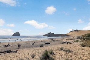 Ein Strand mit Personen, Dünen und einer großen Felsformation.