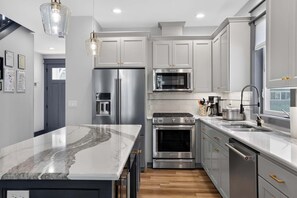 A modern kitchen with stainless steel appliances, a marble countertop, and wooden flooring. - Dory Coastal Paradise - walk to Cape Kiwanda (Pacific City)