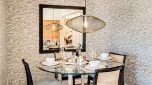A dining area with a round glass table, two wicker chairs, and a large mirror above. - Camps Bay 2 Bed With Sea Views Shoreline Views (Cape Town)