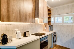 Eine moderne Küche mit Holzschränken, einer eingebauten Mikrowelle, einem Toaster, einem Wasserkocher und einer Waschmaschine.