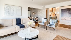 A modern living room with a sofa, chairs, a coffee table, and a dining area with a table and chairs. - Camps Bay 2 Bed With Sea Views Shoreline Views (Cape Town)