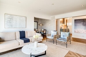 Ein modernes Wohnzimmer mit einer Couch, Sesseln, einem Couchtisch und einem Essbereich mit Tisch und Stühlen.