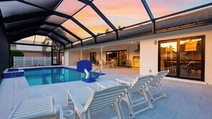 A covered outdoor swimming pool with lounge chairs and a barbecue area. - Latitude 26° Luxury Retreat by Avantstay Waterfall Pool + Private Dock (Fort Myers)