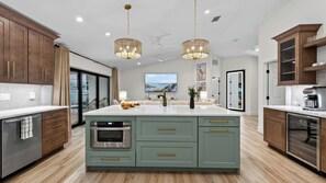 A modern kitchen with a central island, wooden cabinets, and pendant lighting. - Latitude 26° Luxury Retreat by Avantstay Waterfall Pool + Private Dock (Fort Myers)