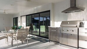 Eine Außenküche mit Grill, Esstisch, Stühlen und Blick auf den Garten.