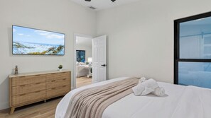 A bedroom with a bed, a dresser, a TV, and a view of a snowy landscape. - Latitude 26° Luxury Retreat by Avantstay Waterfall Pool + Private Dock (Fort Myers)