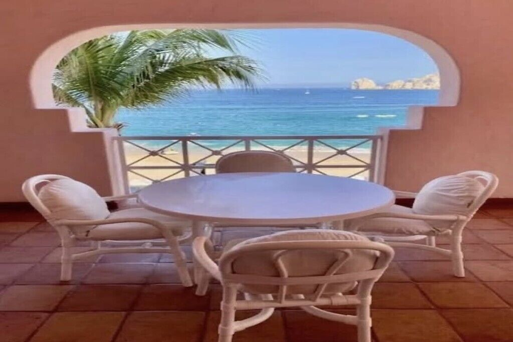 A round table with four chairs, a potted plant, and a view of the sea through an arched window.
