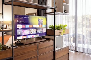 A flat-screen TV mounted on a wooden cabinet with a shelf above displaying various apps and a TV channel menu. - Cómodo y moderno en col. Amerciana Mariachiloft (Guadalajara)