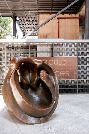 Een sculptuur in een open setting, met een metalen hek en een gebouw op de achtergrond.