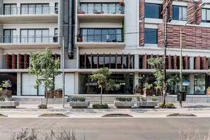 A multi-story building with a modern architectural design, featuring balconies, large windows, and a landscaped entrance area with planters. - Cómodo y moderno en col. Amerciana Mariachiloft (Guadalajara)