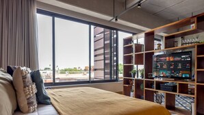 Una moderna camera d'albergo con un'ampia finestra, un letto, una libreria e una televisione a schermo piatto.