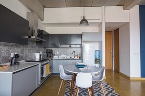 Eine moderne Küche mit grauen Schränken, einem eingebauten Backofen und einem Essbereich mit rundem Tisch und Stühlen.