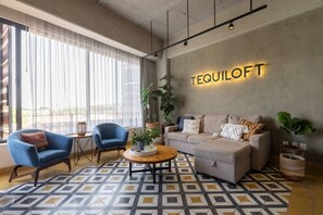 Ein modernes Wohnzimmer mit einer Couch, zwei Sesseln, einem Couchtisch und einem großen Fenster mit durchsichtigen Vorhängen.
