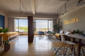 A modern hotel room with a large window, a sofa, a dining table, and a wall-mounted sign reading 'Equiloft'. - Tequiloft arte y esencia Col.Americana@grupo.xingo (Guadalajara)