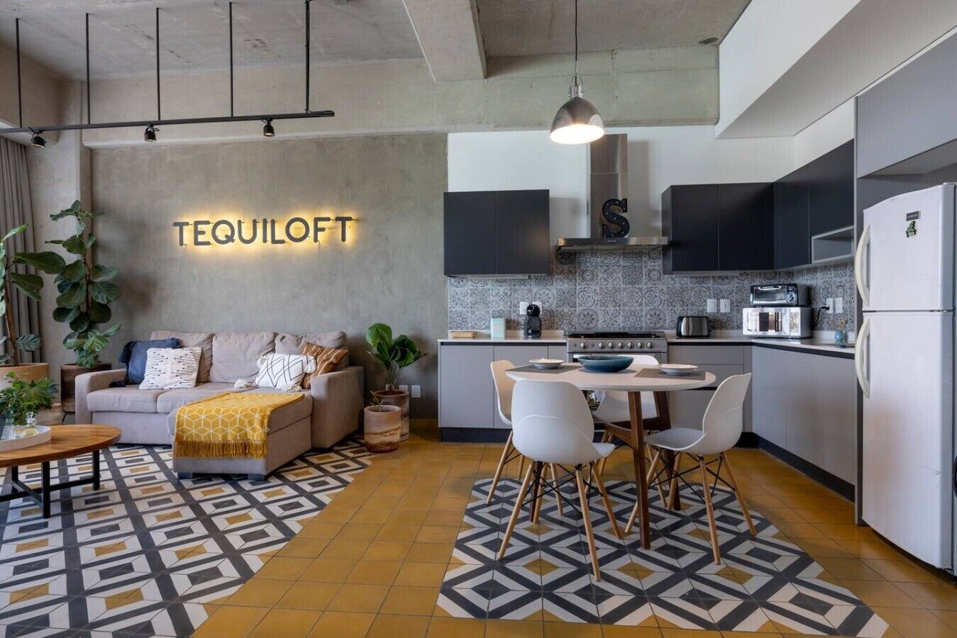Een moderne woonruimte met een bank, salontafel en een eethoek. Een keuken met inbouwapparatuur en een spatwand is zichtbaar.