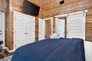 Quarto com paredes de painel de madeira, cama com colcha azul texturizada e duas portas brancas.