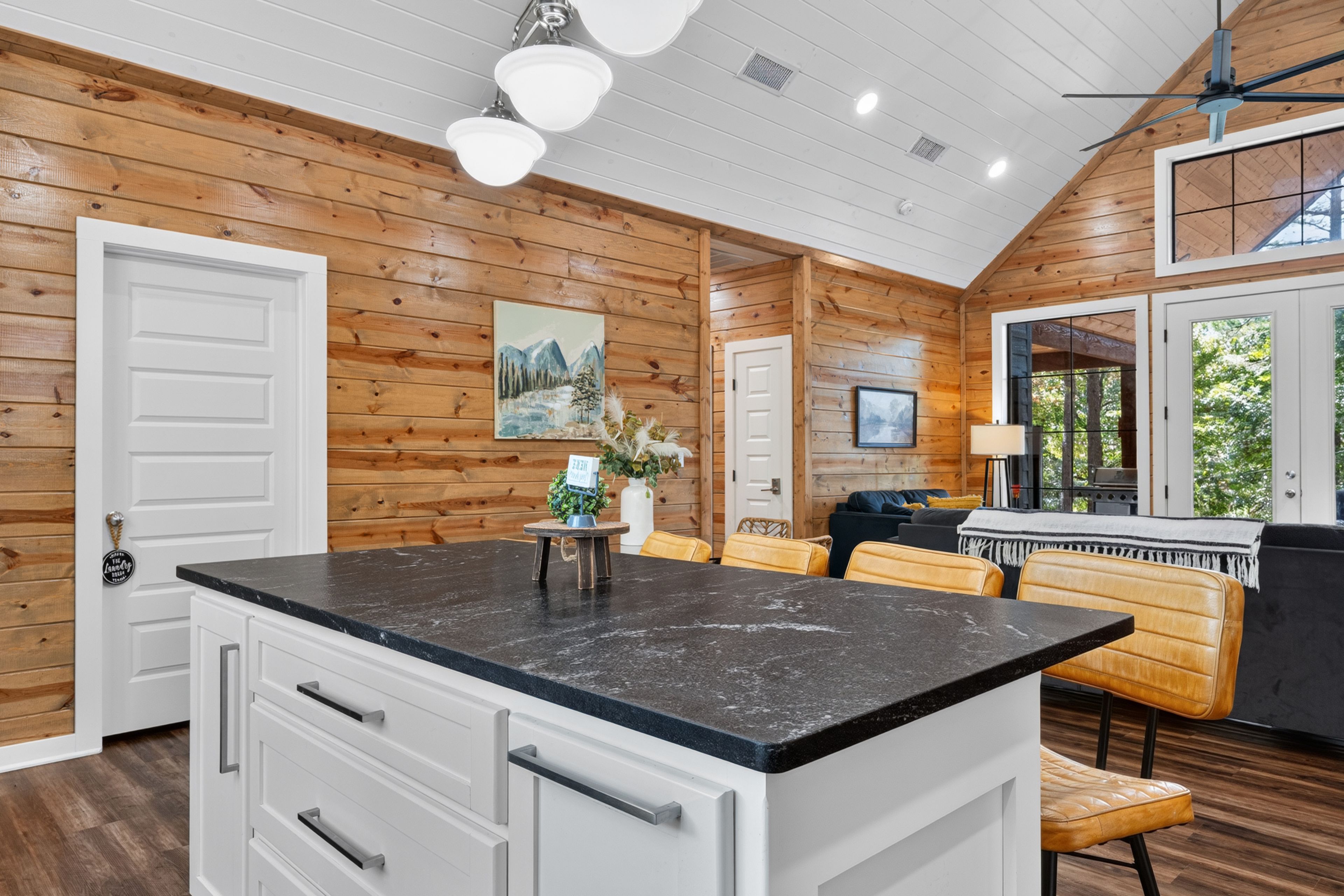 A modern kitchen with a marble countertop, wooden walls, and a dining area with a sofa and chairs.