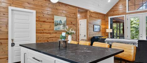 A modern kitchen with a marble countertop, wooden walls, and a dining area with a sofa and chairs.