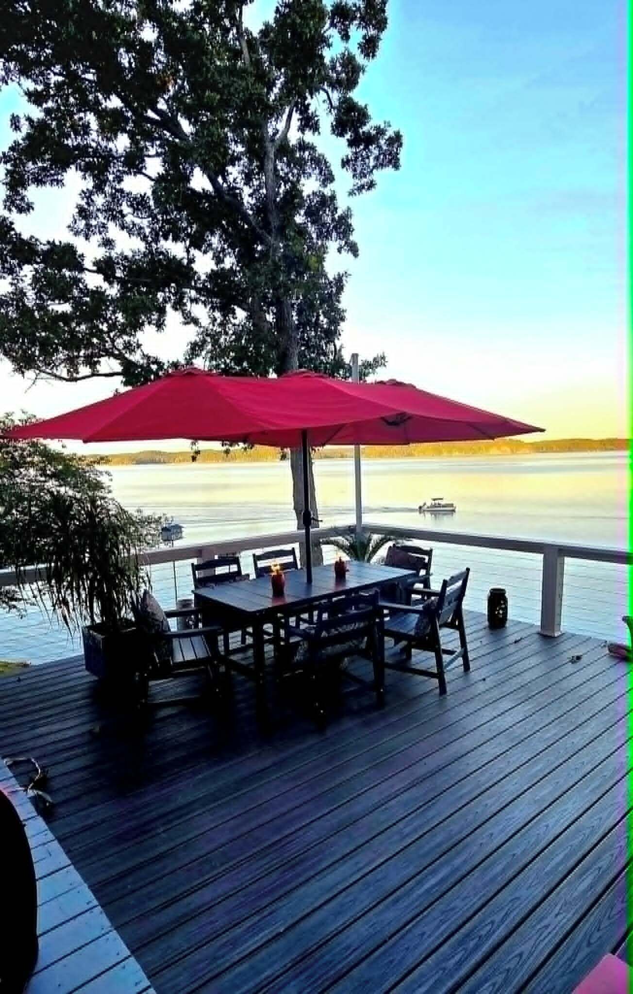 A wooden deck with a table and chairs, an umbrella, and a view of the water.