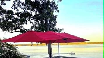 A wooden deck with a table and chairs, an umbrella, and a view of the water.