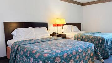 A hotel room with two beds, each with a floral bedspread, a nightstand with a lamp, and a plain wall.