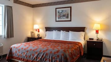 Una habitación de hotel con una cama grande, dos mesitas de noche con lámparas, un cuadro enmarcado en la pared y un ventanal con cortinas.