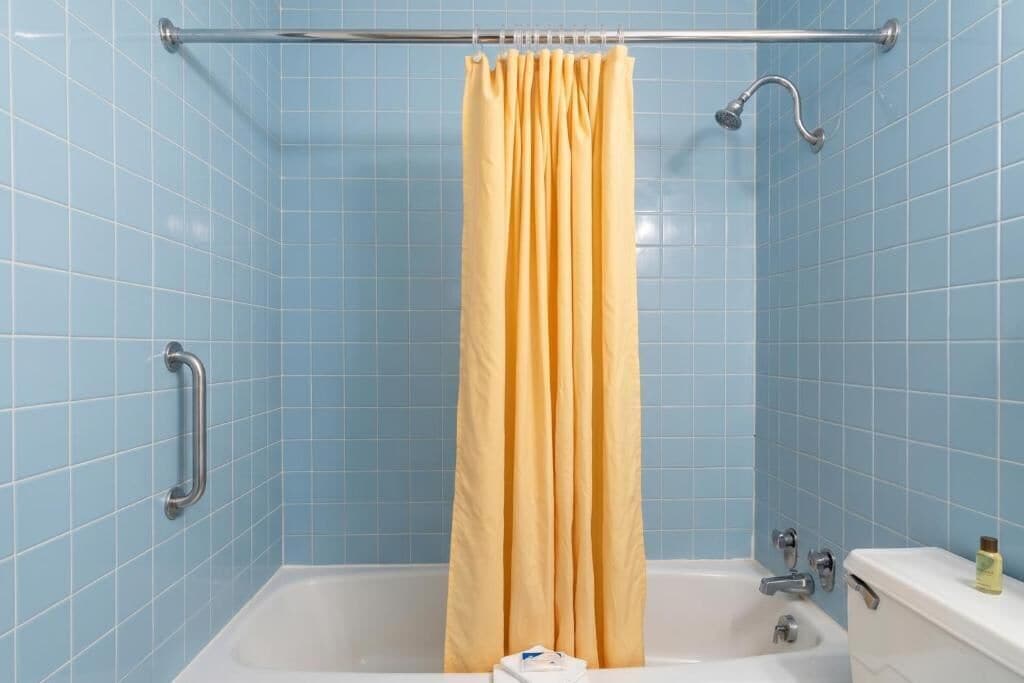 Un baño con bañera, cortina de ducha amarilla y barra de apoyo.