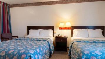 Una habitación de hotel con dos camas, cada una con una colcha estampada con flores, una mesita de noche con lámpara y una silla.
