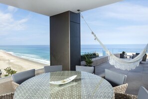 A round glass table with a white centerpiece, surrounded by wicker chairs, overlooking a beach with a hammock. - 2-bedroom condo in superb Cabo San Lucas with AC and gym (Cabo San Lucas)