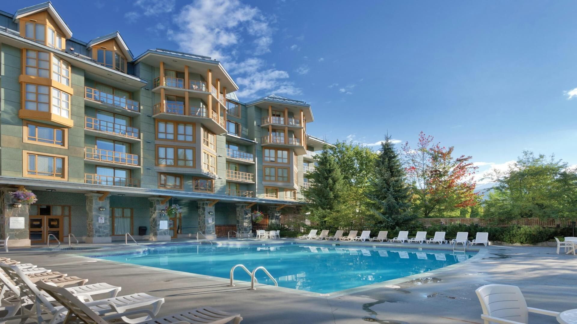 Un hôtel doté d’une piscine, de plusieurs balcons et offrant une vue sur les arbres et les montagnes.