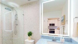 Ein Badezimmer mit einer Duschkabine, einer Toilette, einem Waschbecken mit Marmorplatte und einem großen Spiegel.