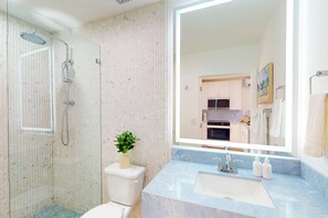 Une salle de bain dotée d’une douche à parois de verre, de toilettes, d’un lavabo avec un plan de toilette en marbre et d’un grand miroir.
