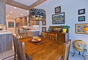 A dining area with a wooden table, chairs, a fruit bowl, and a hanging light fixture. - Stylish Spanish townhome w/ mountain views, pool & spa in South Palm Springs (Palm Springs)