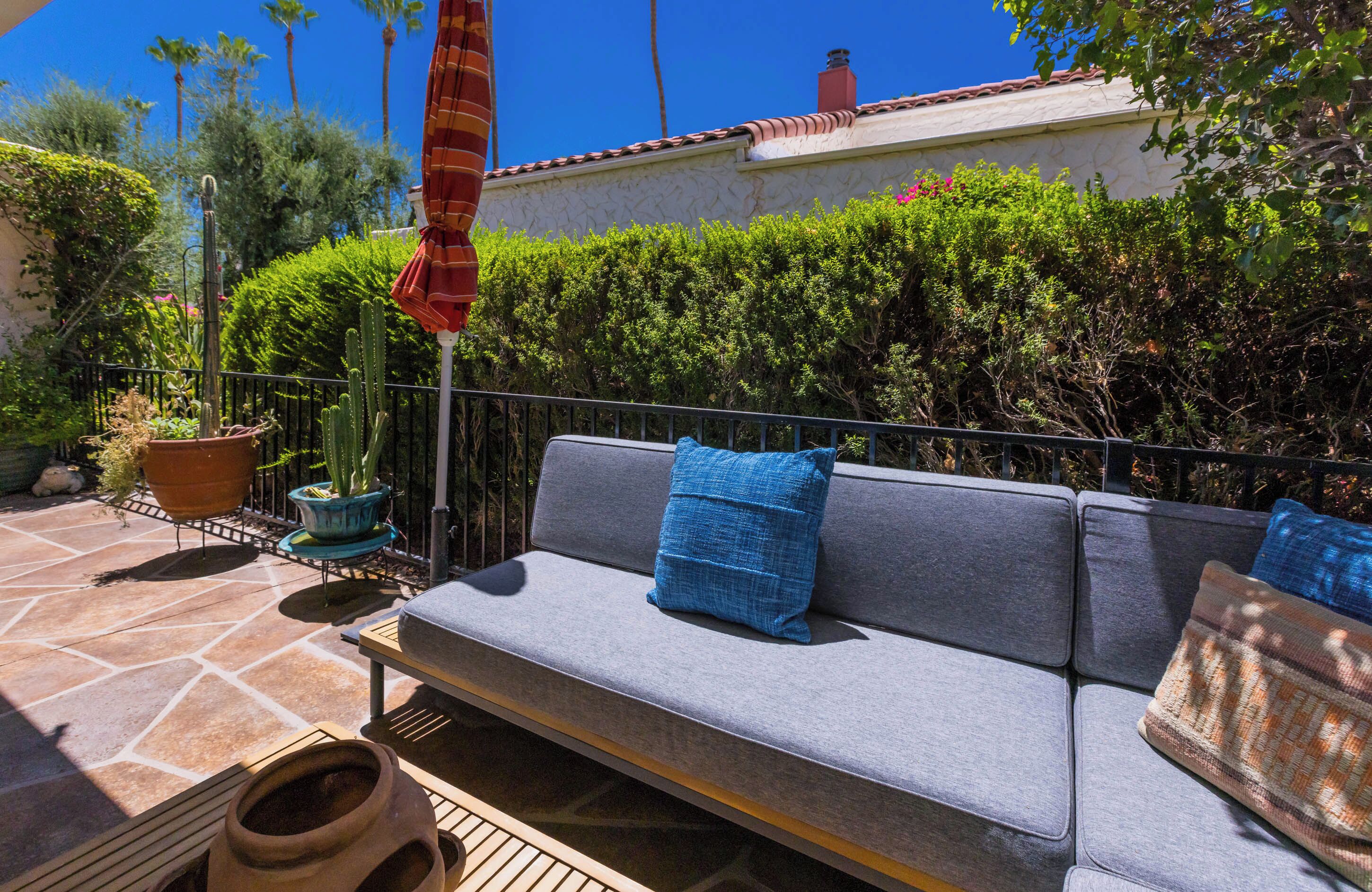 An outdoor seating area with a sofa, cushions, and potted plants.