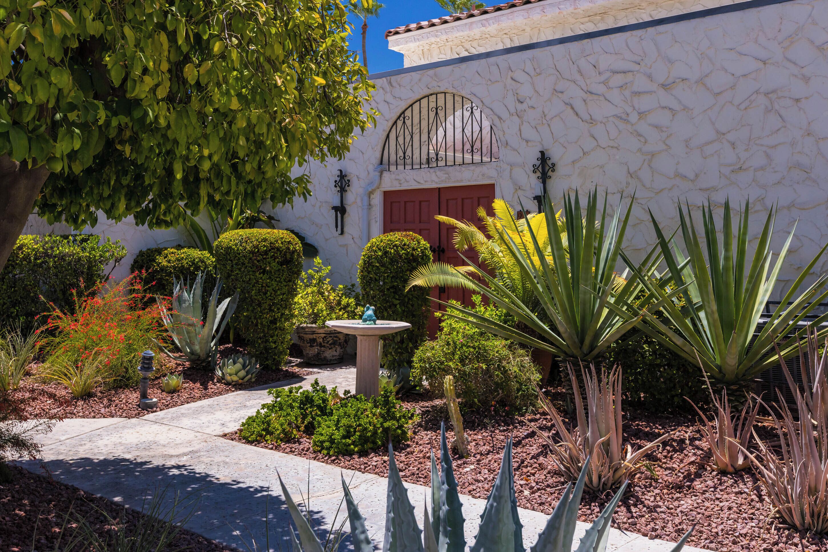 Un jardin bien entretenu, agrémenté de diverses plantes, d’un mur en pierre et d’une porte rouge.