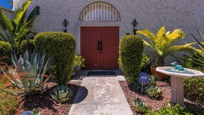 Un edificio con puerta roja, pared de piedra y diversas plantas.